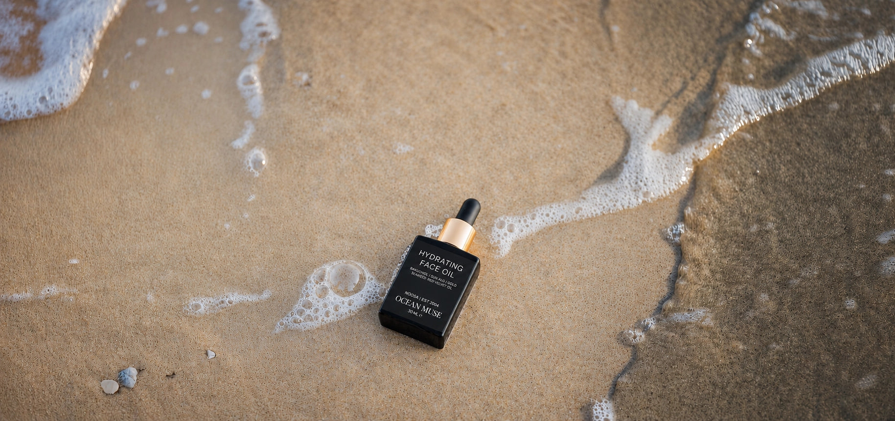 Skincare serum bottle on a sandy beach with ocean waves.