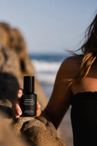 Person holding a bottle of 'Hydrating Youth Serum' by Ocean Mist on a beach.