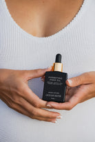 Person holding a black bottle of Ocean Muse Hydrating Face Oil against a white background